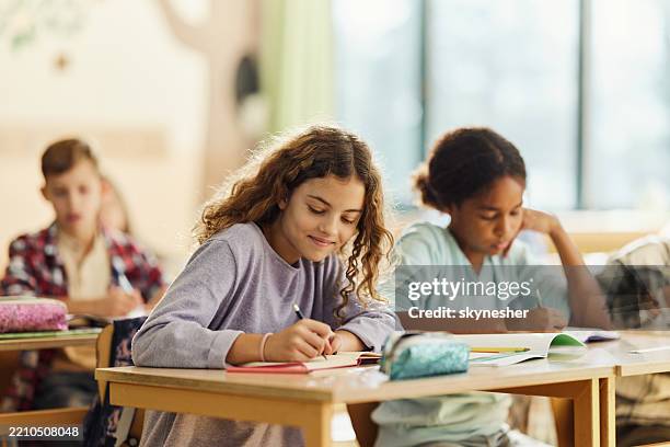 smiling schoolgirl writing on a class at elementary school. - elementary school building stock pictures, royalty-free photos & images