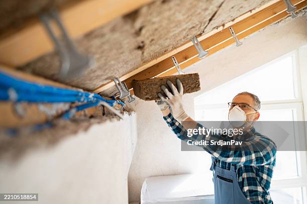 worker installing insulation in attic with mineral wool for improved energy efficiency - isolatiemateriaal stockfoto's en -beelden