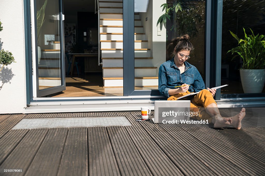 Woman working on a terrace at home with a notebook and laptop