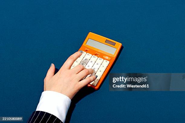 closeup of a hand using a retro orange calculator on a blue background - retro calculator stock pictures, royalty-free photos & images