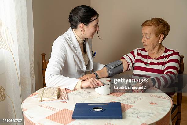 jeune femme, médecin mesurant la tension artérielle d’une femme âgée à domicile - manomètre de pression photos et images de collection