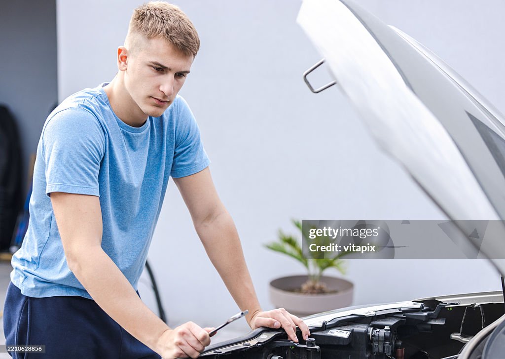 Hombre joven inspeccionando el motor del coche en un entorno urbano al aire libre