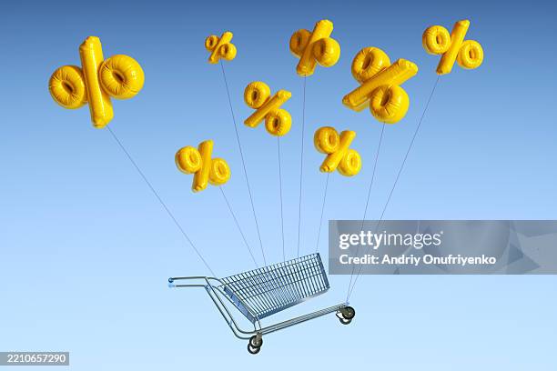 yellow percentage sign balloons lifting empty shopping cart into the air. inflation, tarriff concepts, high cost of living. - ausverkauf stock-fotos und bilder