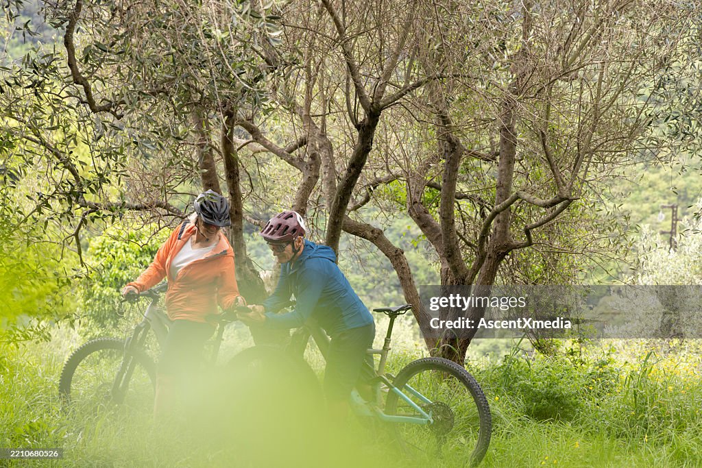 Mature couple e-bike in green olive grove, check direction