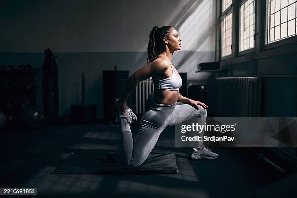 a young woman stretching her quadriceps during a workout session at the gym - quadriceps muscle stock pictures, royalty-free photos & images