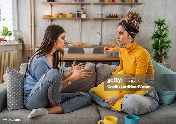 two young women having argument while sitting on sofa at home - friends fighting stock pictures, royalty-free photos & images