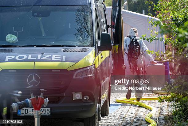 An investigator wearing a protective suit carries boxes in a street blocked off by police following the raid of a possible ricin lab at a residence...