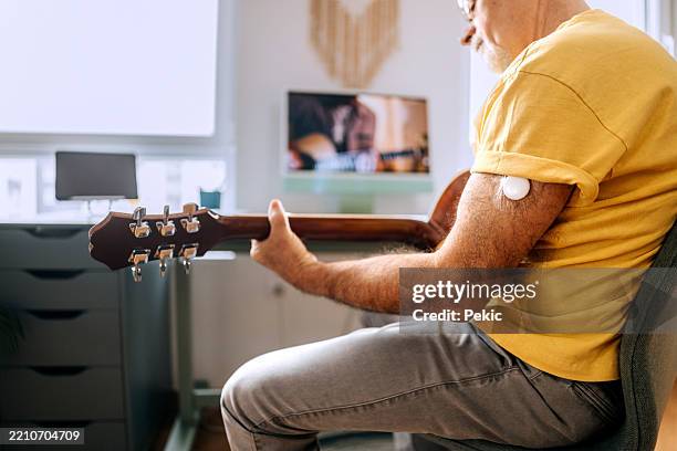 älterer mann, der videos auf einem desktop-pc anschaut, während er gitarre spielen lernt - typ 1 diabetes stock-fotos und bilder