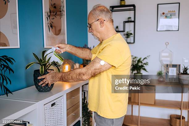 senior man watering plants at home - continuous glucose monitor stock pictures, royalty-free photos & images