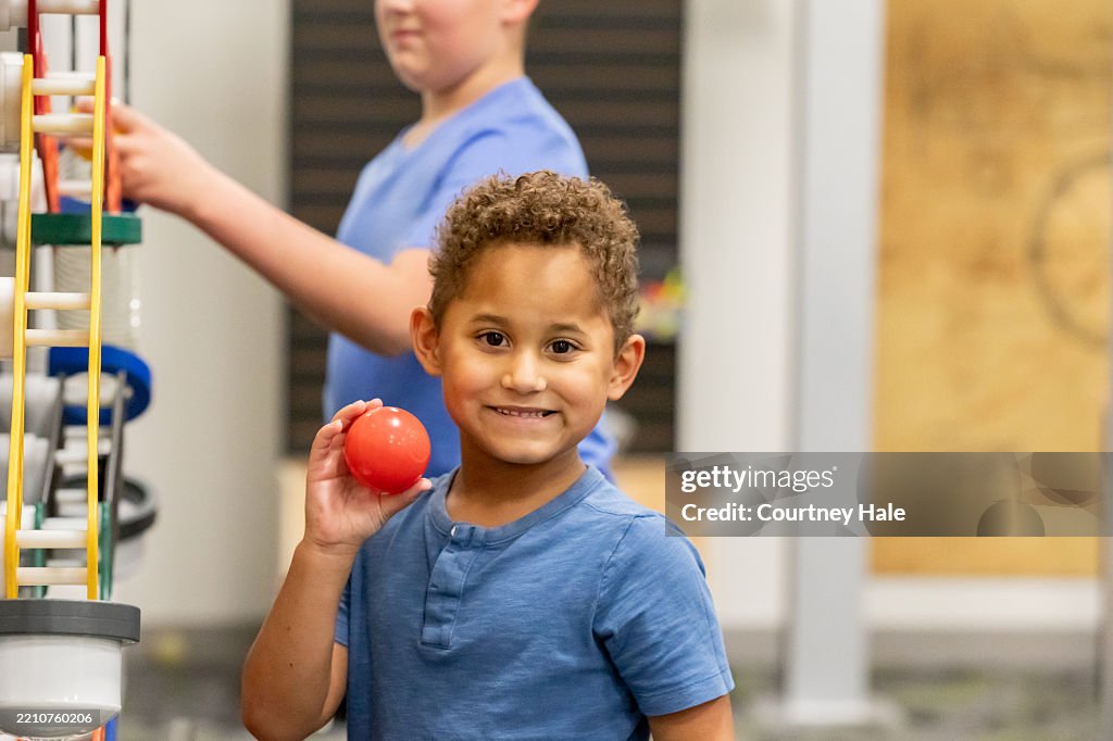 Adorable little boy holds ball while using educational toys in STEM classroom