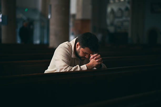 young man sitting on the pews of the dark church, profile portrait in a religious interior - christian love stock pictures, royalty-free photos & images
