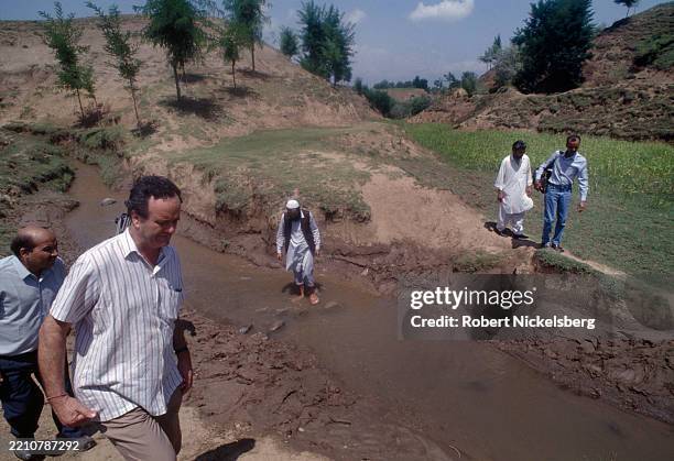 View of journalists, including BBC Radio correspondent Mark Tully and unidentified members of a television crew, as they walk along a creek, Budgam,...