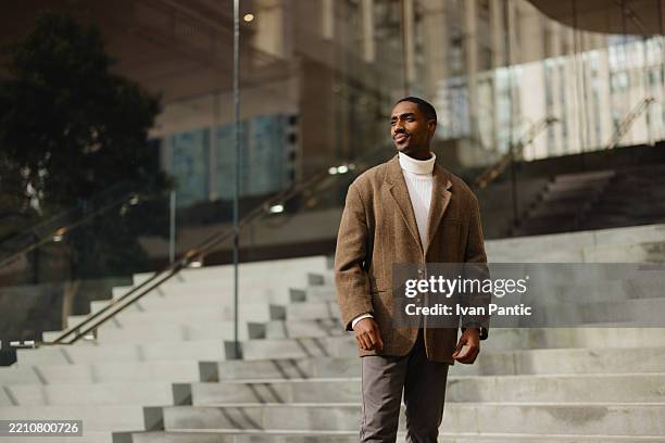 stylish man in brown jacket standing on modern urban steps outdoors - menswear stock pictures, royalty-free photos & images