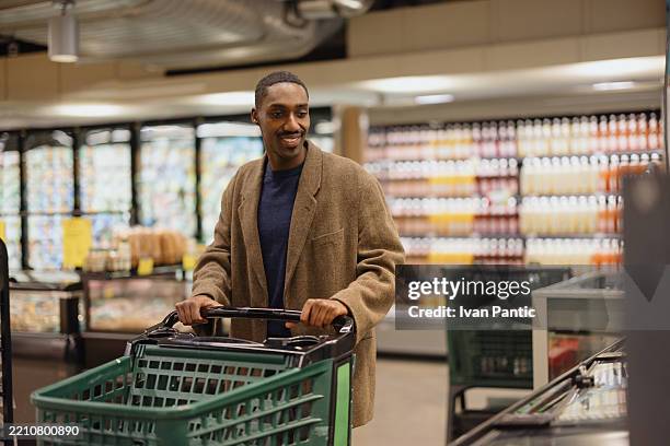 man smiling while shopping in a grocery store with a shopping cart - digital-directory stock pictures, royalty-free photos & images