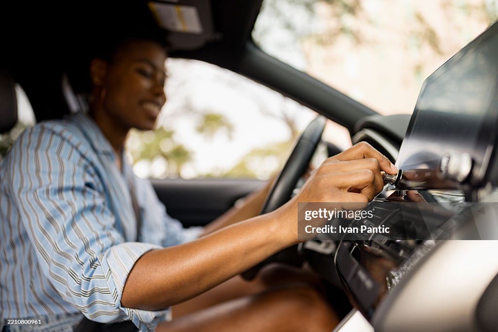 Mujer ajustando los controles de audio del automóvil mientras está sentada en el asiento del conductor
