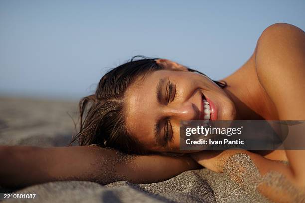 donna sorridente che si rilassa sulla spiaggia sabbiosa sotto la calda luce del sole - caratteristica della pelle foto e immagini stock