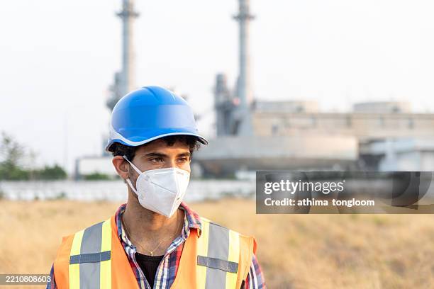 close-up of a male engineer wearing protective face mask with power plant background. - respiratory protection construction stock pictures, royalty-free photos & images
