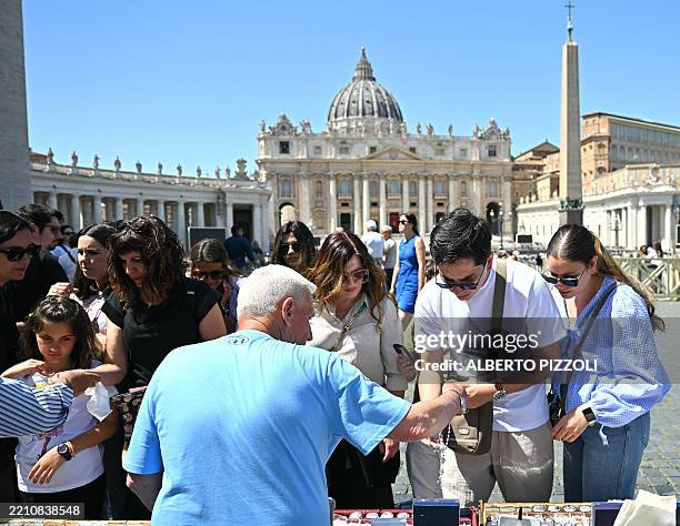 Visitors buy souvenirs from an authorised street vendor near St Peter's Square with the St Peter's basilica and the Apostolic palace in the...