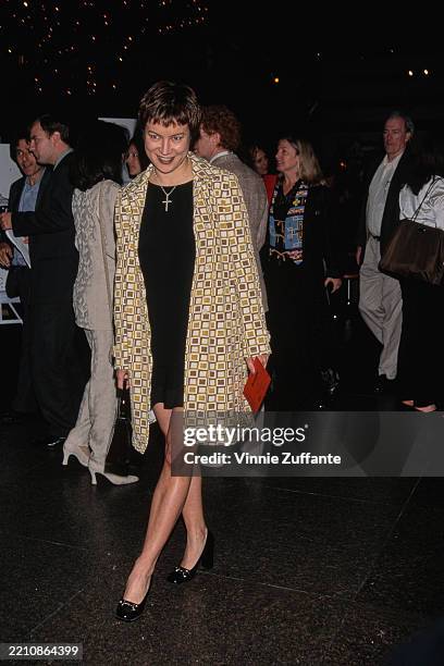 American-Canadian actress Jennifer Tilly, wearing a yellow-and-brown pattern coat over a black minidress, with a crucifix hanging from a necklace,...
