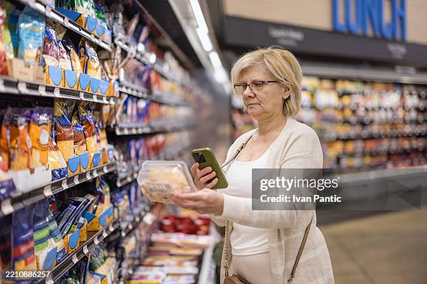 donna che fa la spesa nel corridoio del negozio di alimentari utilizzando lo smartphone per le informazioni sul prodotto - cibo precotto foto e immagini stock