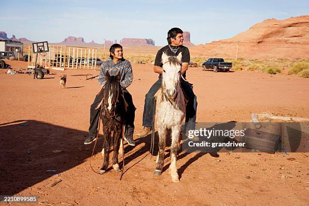 navajo siblings riding horses together on a family ranch in the desert of monument valley arizona - indianenreservaat stockfoto's en -beelden