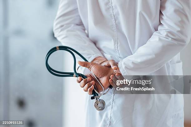 doctor holding a stethoscope behind their back in a clinical setting - phonendoscope stock pictures, royalty-free photos & images