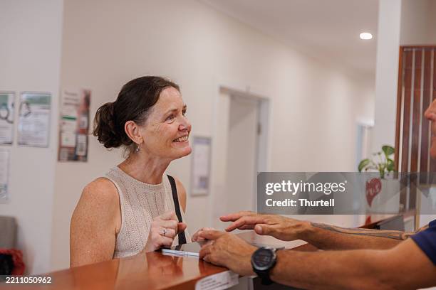 female patient checking in at reception of medical centre using a digital tablet - medicare stock pictures, royalty-free photos & images