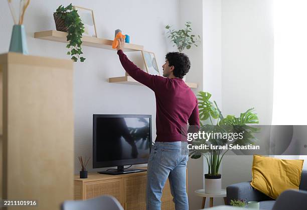 man cleaning shelves in living room - spolverare foto e immagini stock