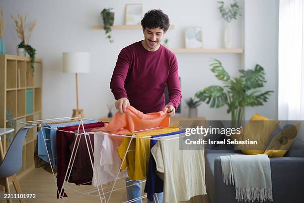 smiling man hanging clean laundry at home - wäscheständer stock-fotos und bilder
