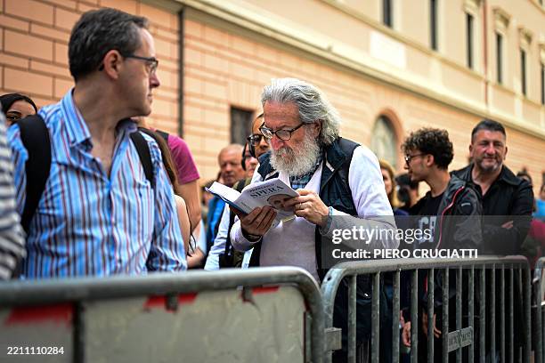 Graphic content / A man reads Pope Francis' autobiography "Hope" while lining up with mourners and visitors to pay their respects to the late Pope...