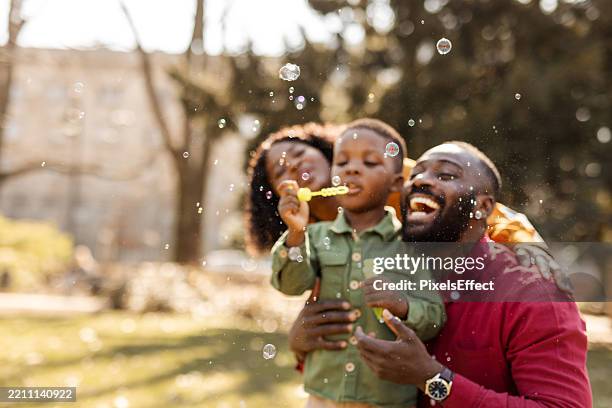 feliz familia afroamericana soplando burbujas al aire libre - familia de verdad fotografías e imágenes de stock