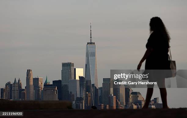 The sun sets on the skyline of lower Manhattan and One World Trade Center in New York City as a person walks in a park on April 20 in Weehawken, New...
