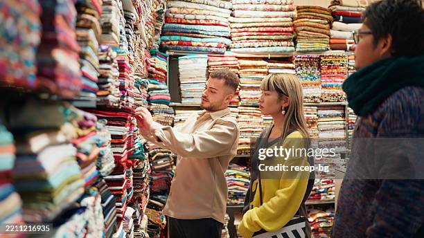 verkäuferin im souvenirshop, die kunden in einem textil-souvenirshop mit den stoffen hilft - souvenir stock-fotos und bilder