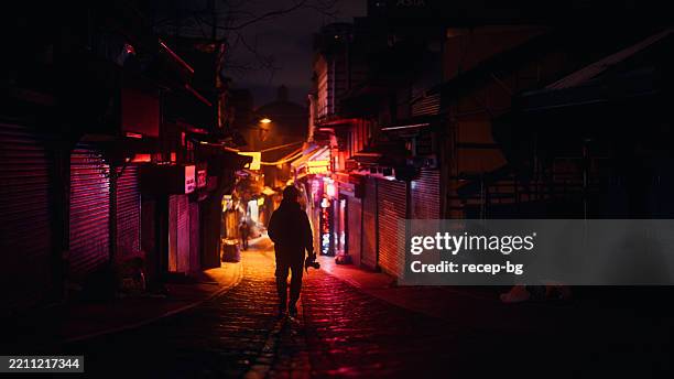 hombre viajero solitario caminando en un pequeño callejón iluminado por farolas y letreros de neón por la noche - callejuela fotografías e imágenes de stock