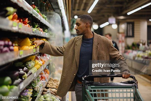 african american man buying fresh vegetables at greengrocer's shop. - healthy eating stock pictures, royalty-free photos & images
