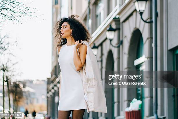 chic woman in city. young interracial businesswoman walking with jacket over shoulder - sleeveless dress stock pictures, royalty-free photos & images