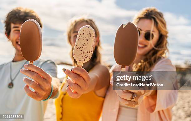 young friends showing ice cream on a sunny beach - ice cream stock pictures, royalty-free photos & images