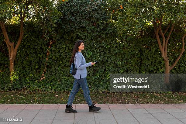 person walking in a park with a smartphone and backpack - botas fotografías e imágenes de stock