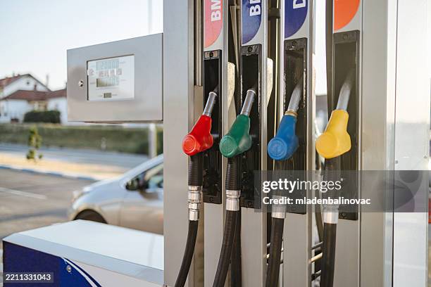 surtidores de combustible colgados en la bomba de la estación de servicio con un automóvil esperando en el fondo - bomba de combustible fotografías e imágenes de stock