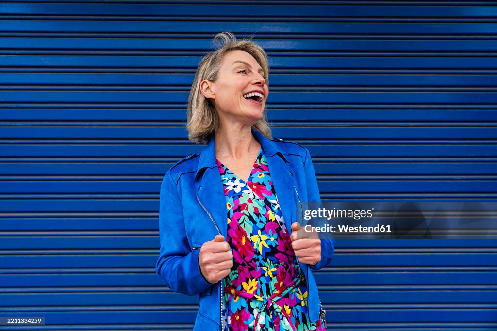 Smiling person in a colorful dress and blue jacket on an urban street