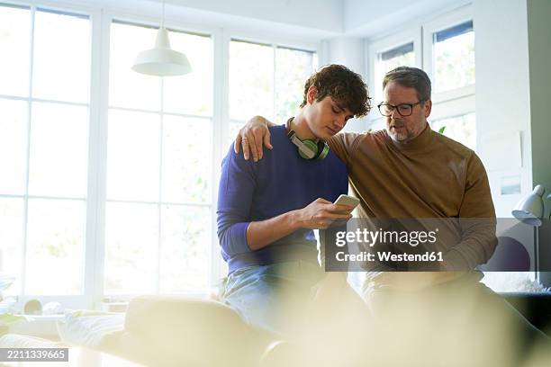 father and son bonding at home while using a smartphone - 18 19 años fotografías e imágenes de stock