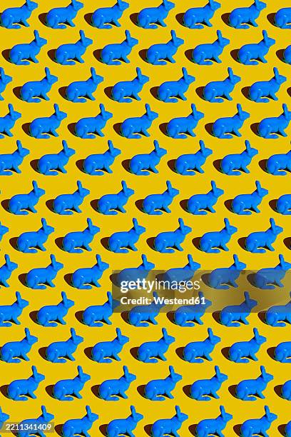 blue plastic rabbits forming a pattern on a yellow background - herd stock illustrations