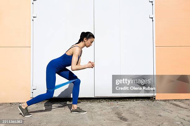 young woman in a blue leotard working out with a rubber band at big white doors in a peach wall. - gym entrance exterior stockfoto's en -beelden