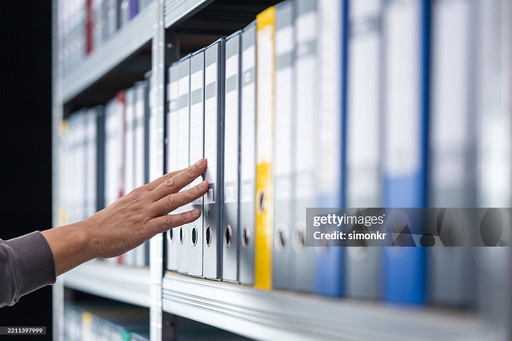 Human Hand Reaching Toward Archived File on Office Shelf