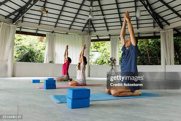 people practicing yoga in a serene pavilion surrounded by lush greenery - retreating stock pictures, royalty-free photos & images