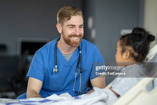 young girl smiling while interacting with a caring hospital nurse - male nurse stock pictures, royalty-free photos & images