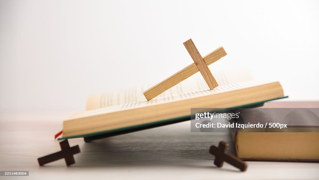Open Bible on wooden table with several wooden crosses