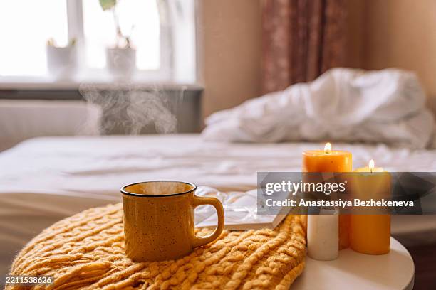 yellow mug with hot drink on a soft blanket next to candles against the background of a white bed, cozycore - hygge stockfoto's en -beelden