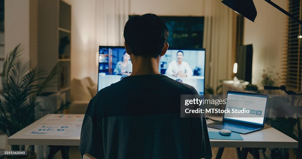 Young Asian video conference late at night from home office, financial documents and discussing with colleagues online, showcasing remote teamwork and dedication. Remotely and finance.