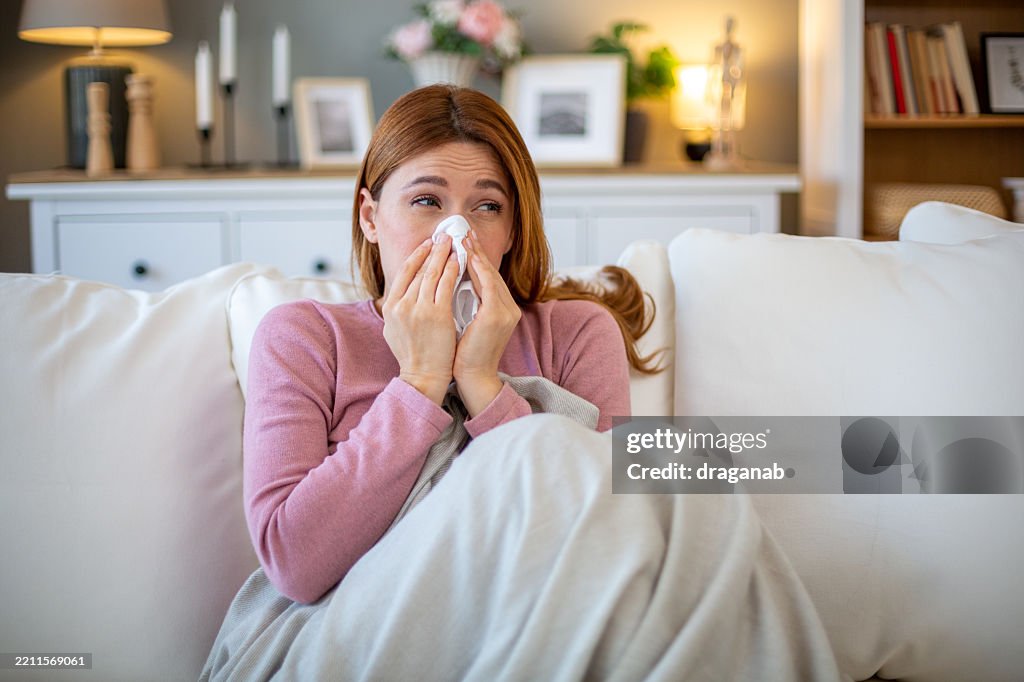 Sick woman blowing nose while sitting on sofa at home